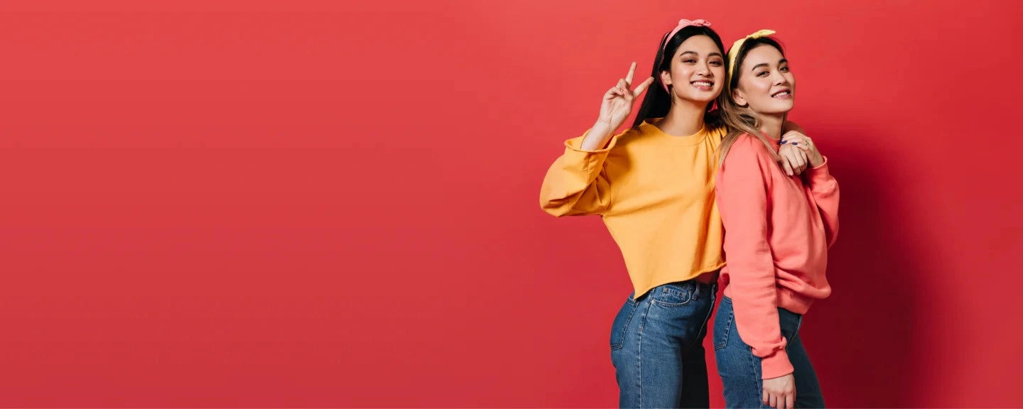 Two young women in bright casual outfits smiling with energy and confidence, representing the benefits of vitamin B12 for an active lifestyle.